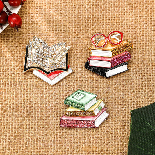 Three book-shaped pins on a textured fabric background