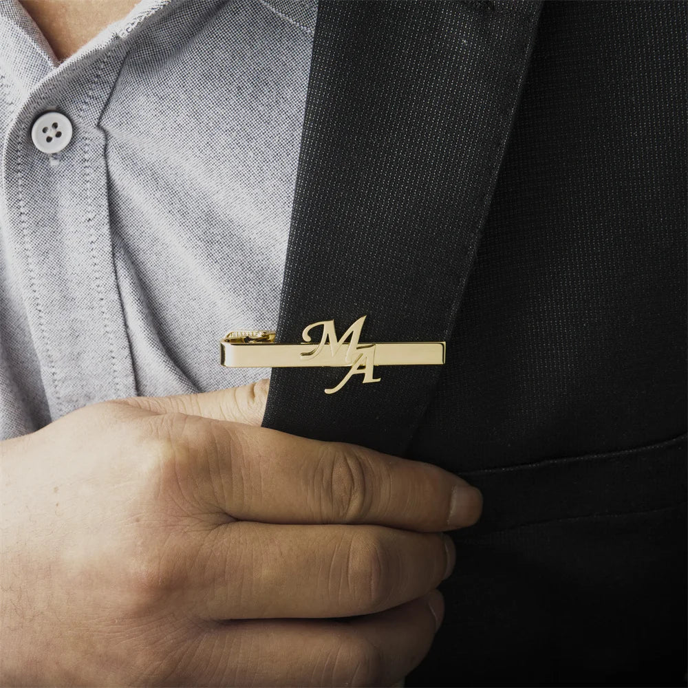 Custom gold tie clip with initials on a black tie.