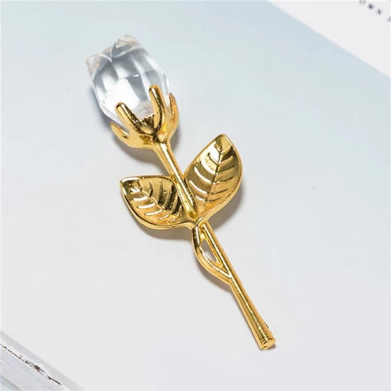 Gold rose-shaped object with a clear crystal on a light gray background