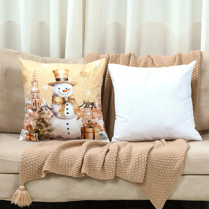 Decorative pillow with a snowman design on a beige couch with a white pillow and beige blanket.