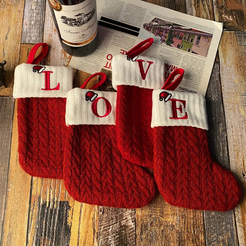 Four red knitted Christmas stockings with 'LOVE' on a wooden surface.