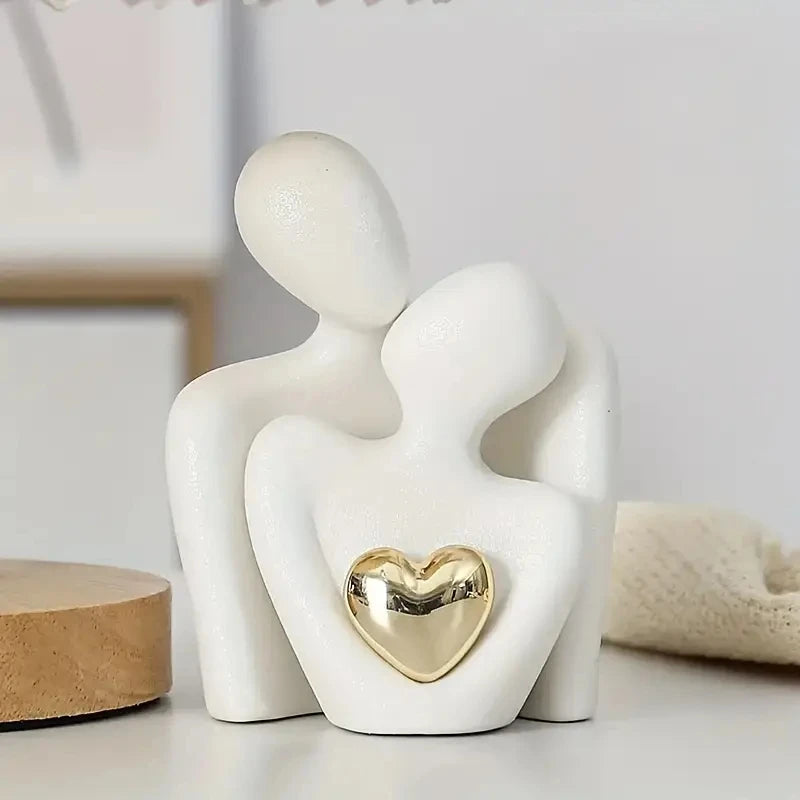 White sculpture of two figures embracing with a gold heart detail on a light background