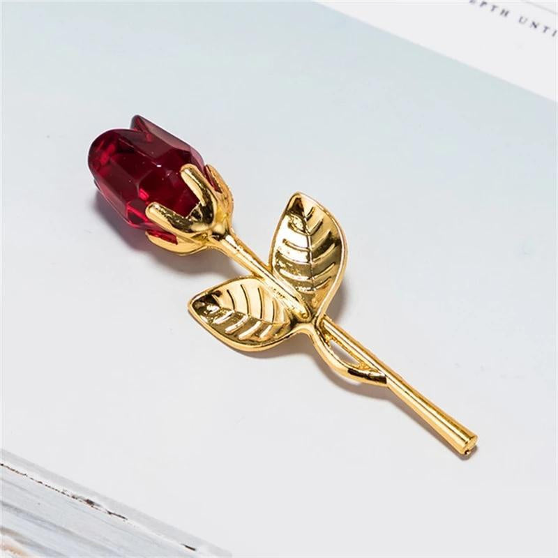 Gold rose with a red gemstone on a light background
