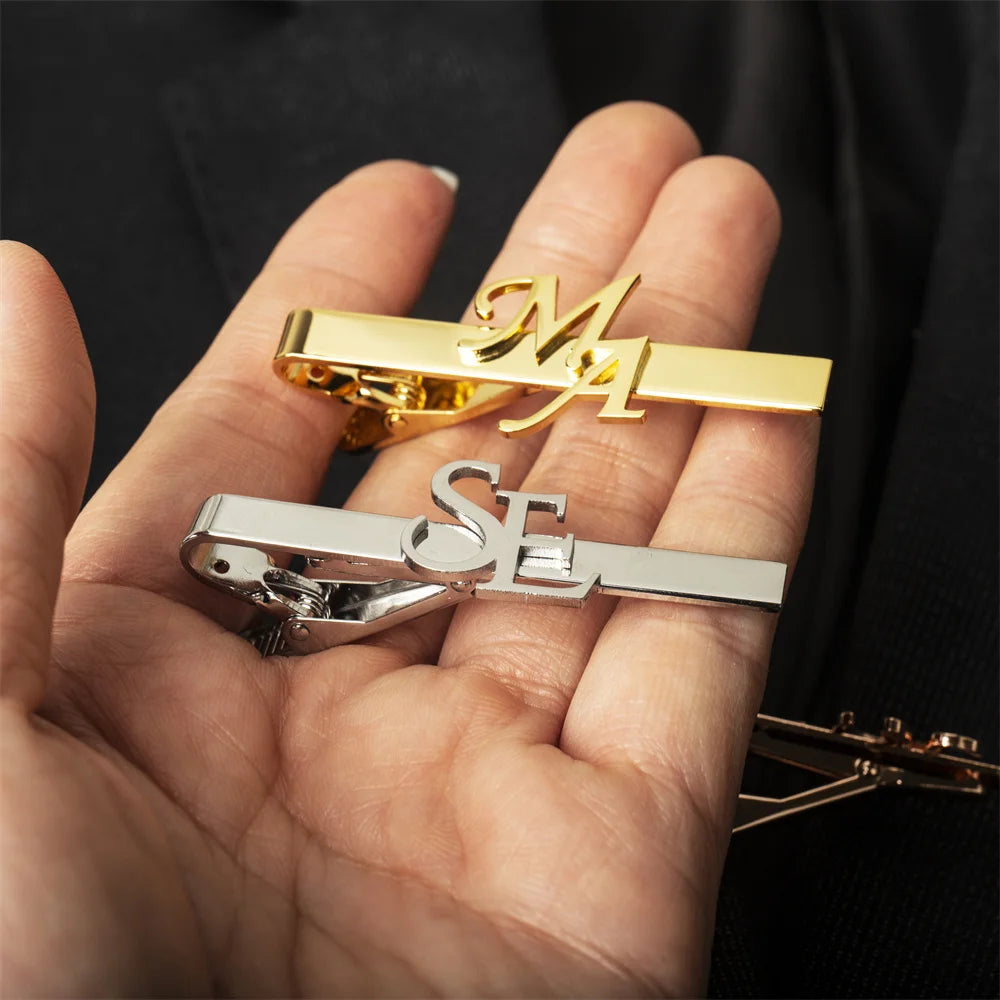 Gold and silver tie clips held in a hand against a dark background