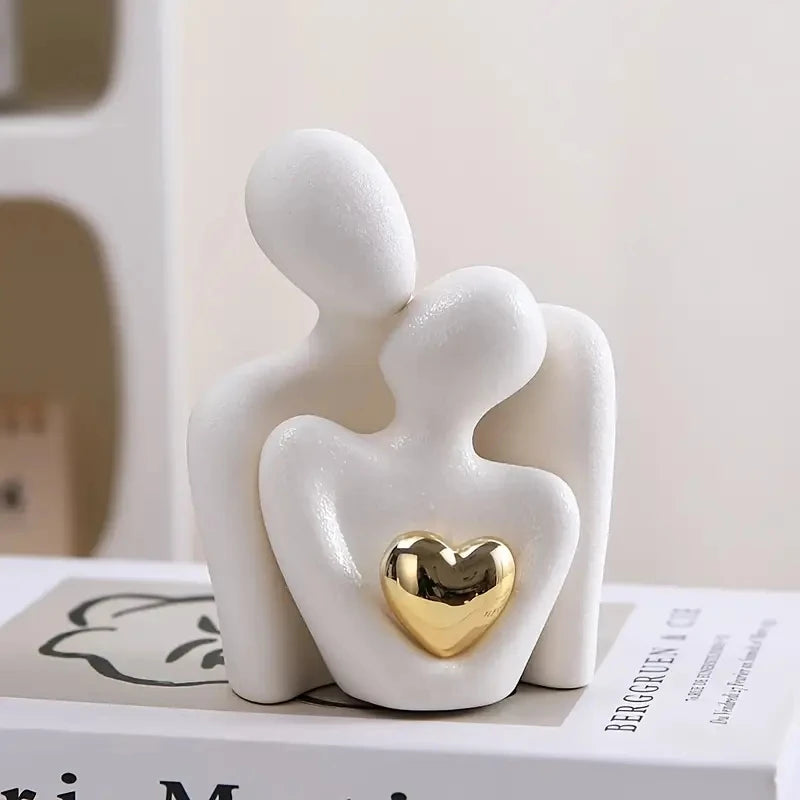 White figurine of two people holding a gold heart on a white surface.