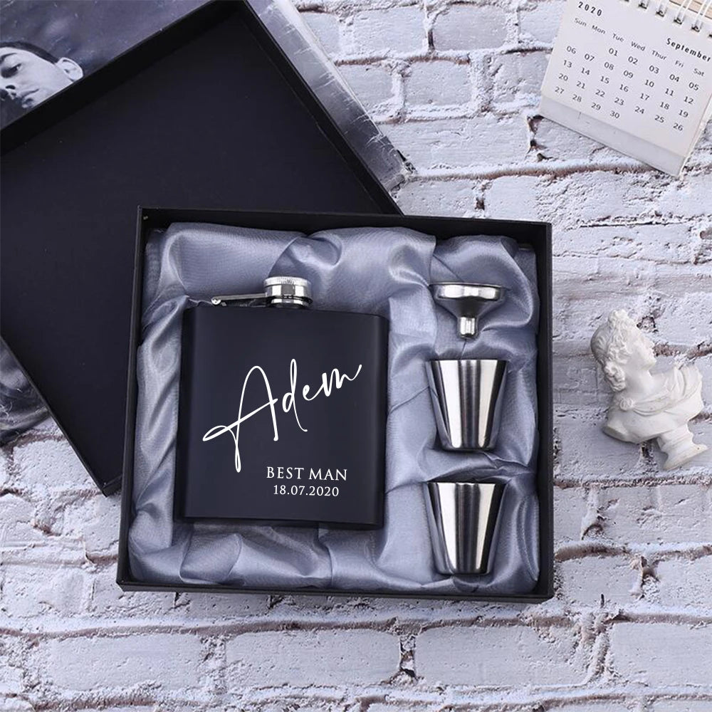 Personalized black flask set with silver components in a gift box on a textured wall background.