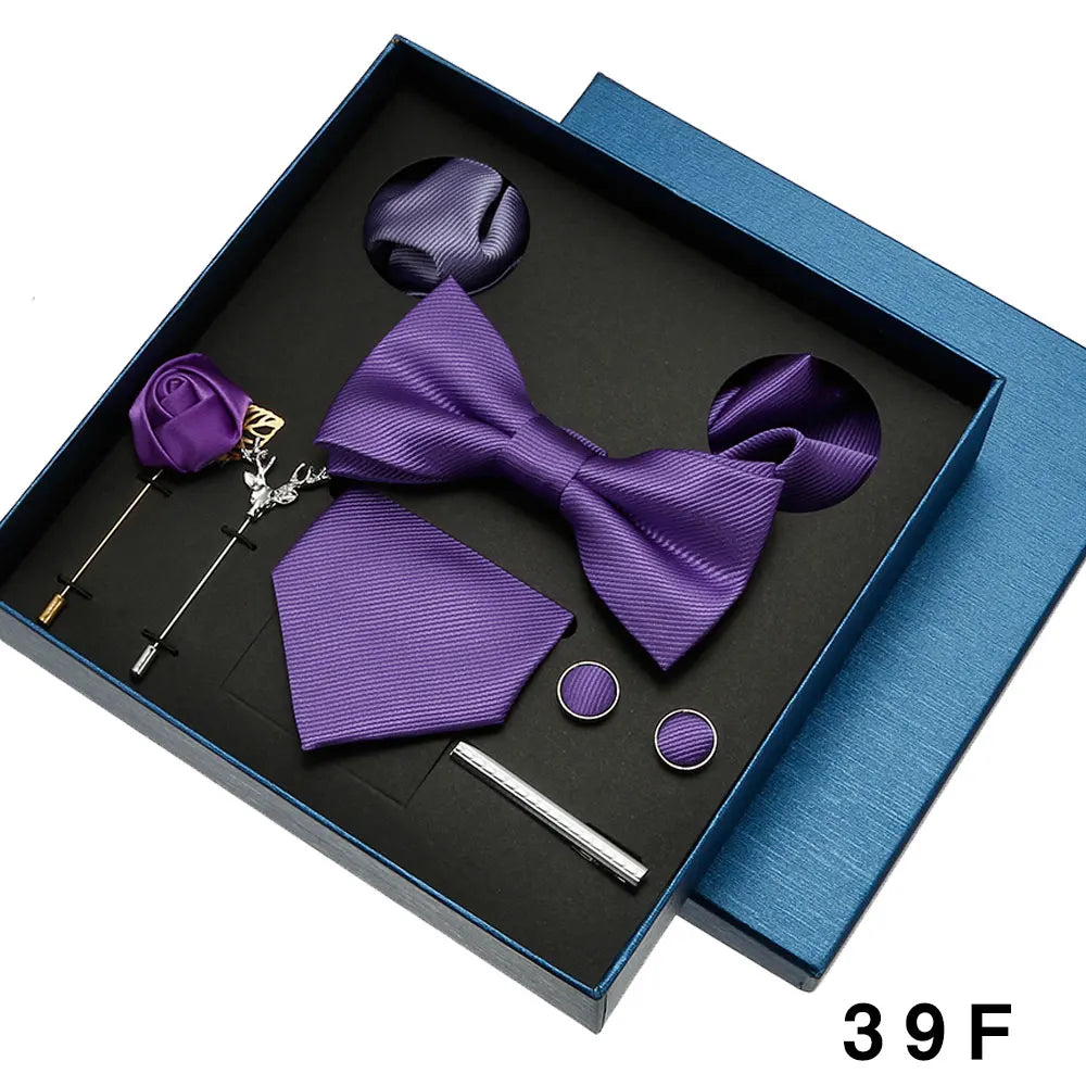 Purple bow tie and pocket square set with accessories in a black box on a white background