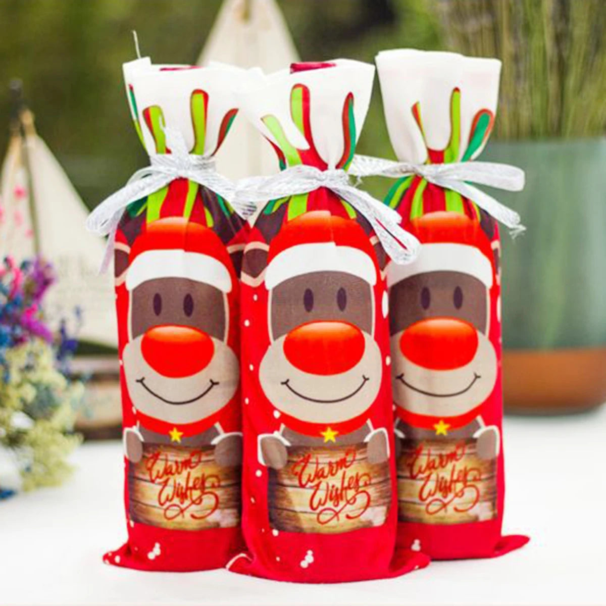 Three red bottles with reindeer faces and 'Merry Christmas' text, wrapped in festive bag.