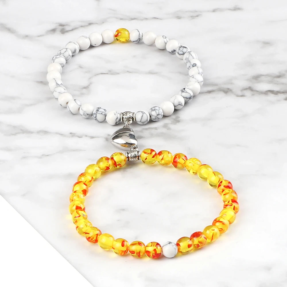 Two beaded bracelets, one with white and yellow beads and the other with orange and yellow beads, on a marble surface.