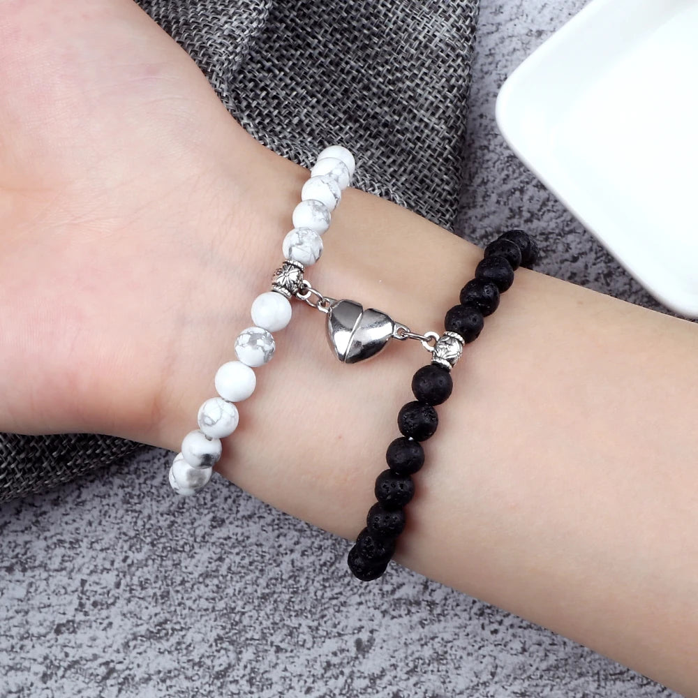 Two bracelets on a wrist, one white with silver heart charm and one black beaded bracelet.
