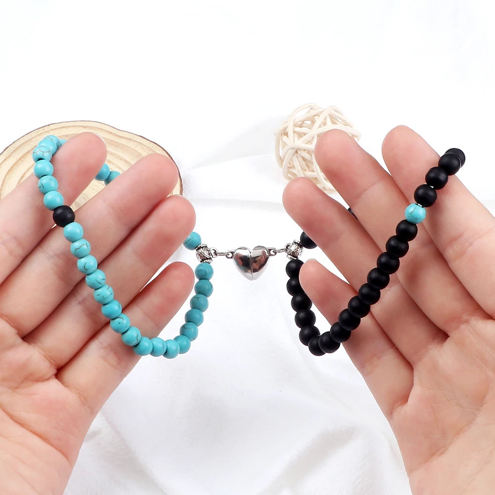 Two beaded bracelets, one turquoise and one black, held in hands against a white background.