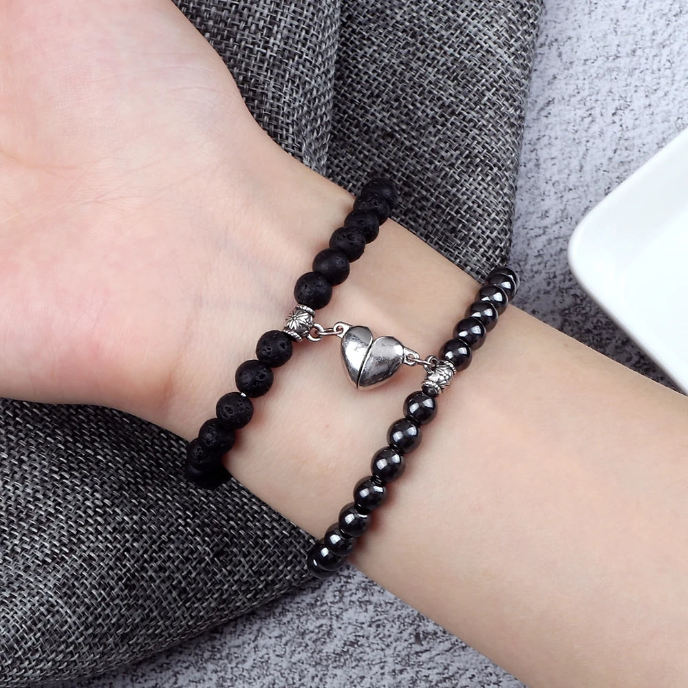 Black beaded bracelet with a silver heart charm on a wrist against a gray fabric background